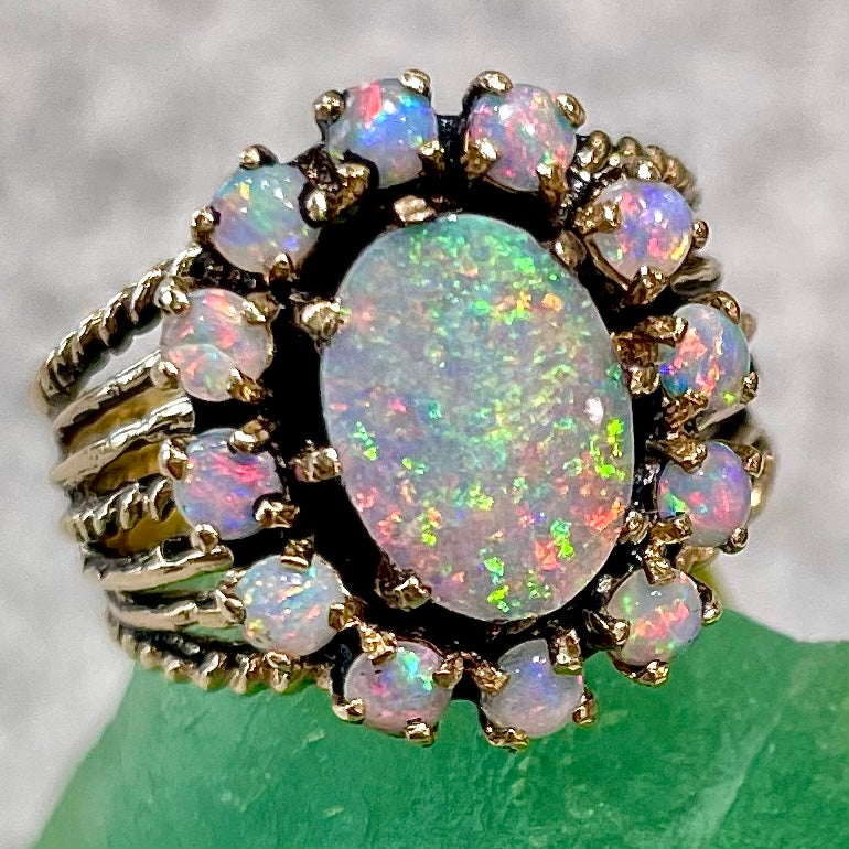 Vintage yellow gold oval opal cabochon ring set with 12 round opals in a halo around the center stone.