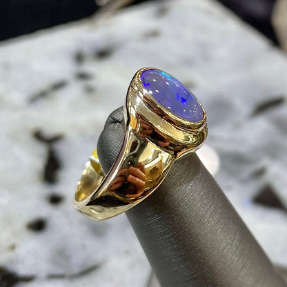 A yellow gold ring set with diamonds and a Lightning Ridge black opal from Australia.
