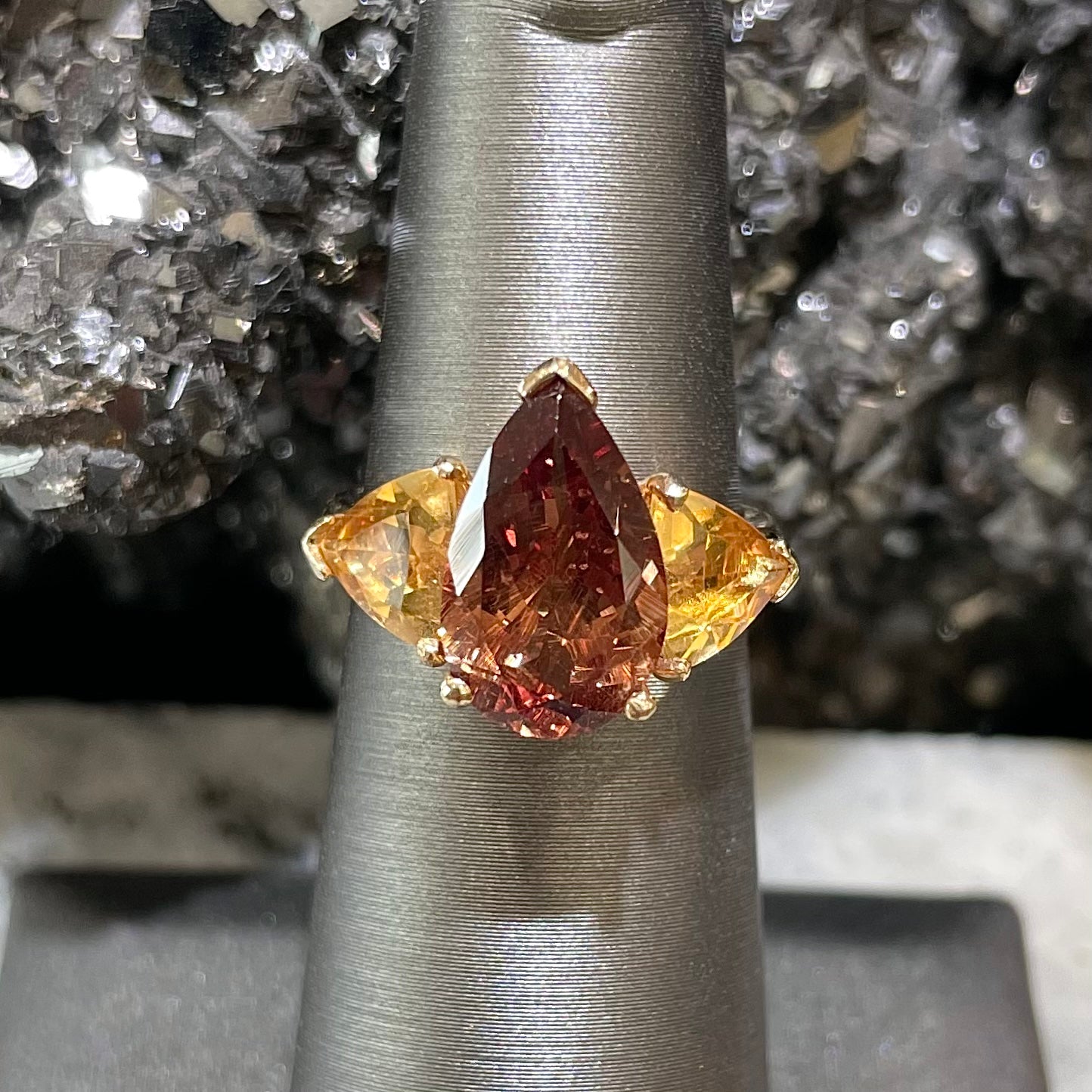 A gold ring set with a pear shape color change garnet between two trillion cut citrine accent stones.