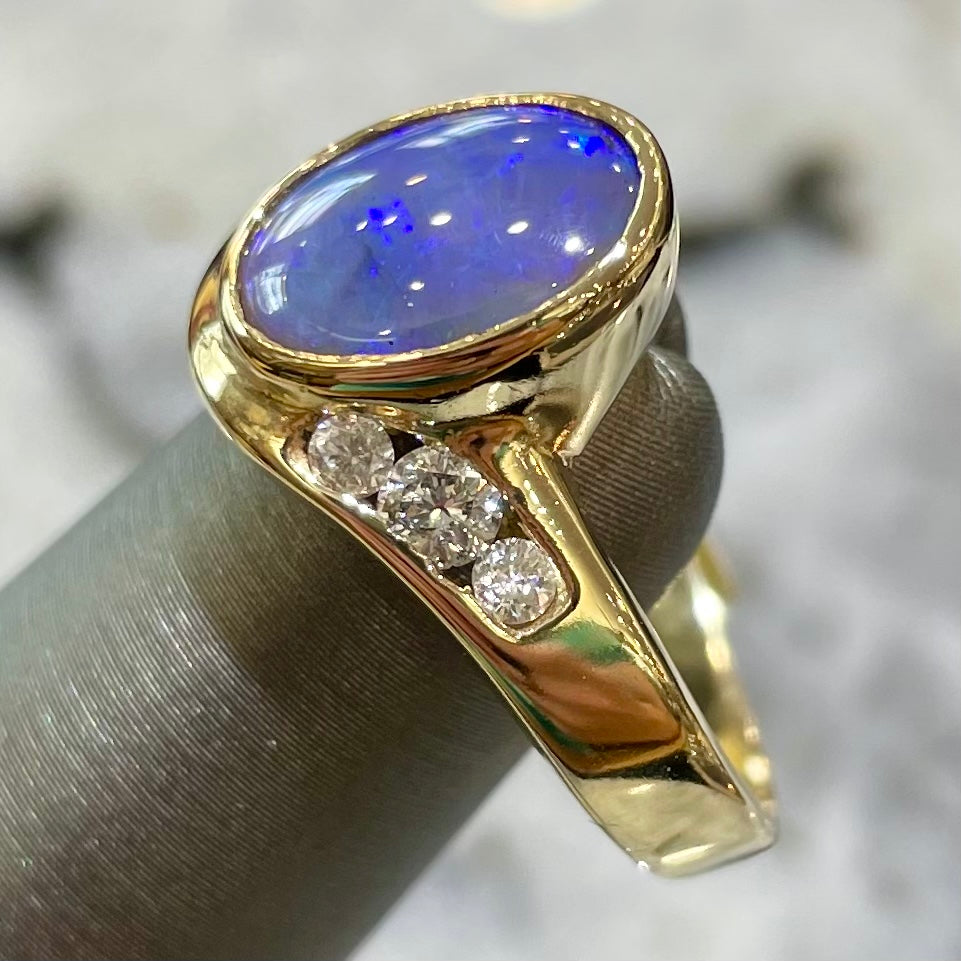 A yellow gold ring set with diamonds and a Lightning Ridge black opal from Australia.