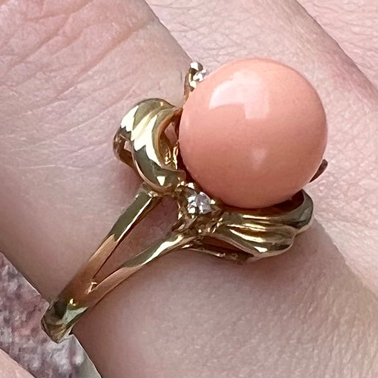 A vintage split shank flower ring set with a round pink coral sphere and diamond accents.