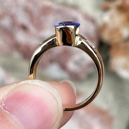 A yellow gold ring half-bezel set with an oval cut blue tanzanite and two flush set round diamonds.