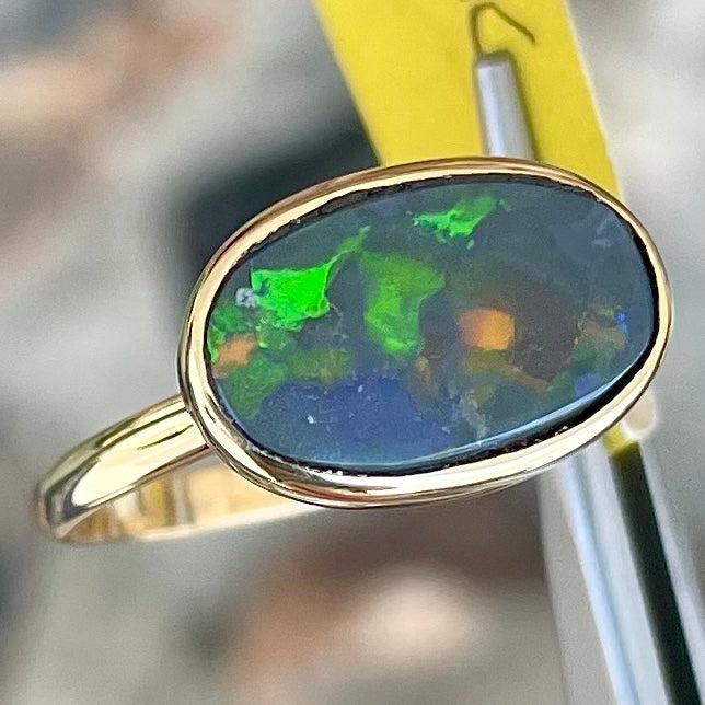 A handmade Lightning Ridge black opal solitaire ring in yellow gold.  Fire is green.