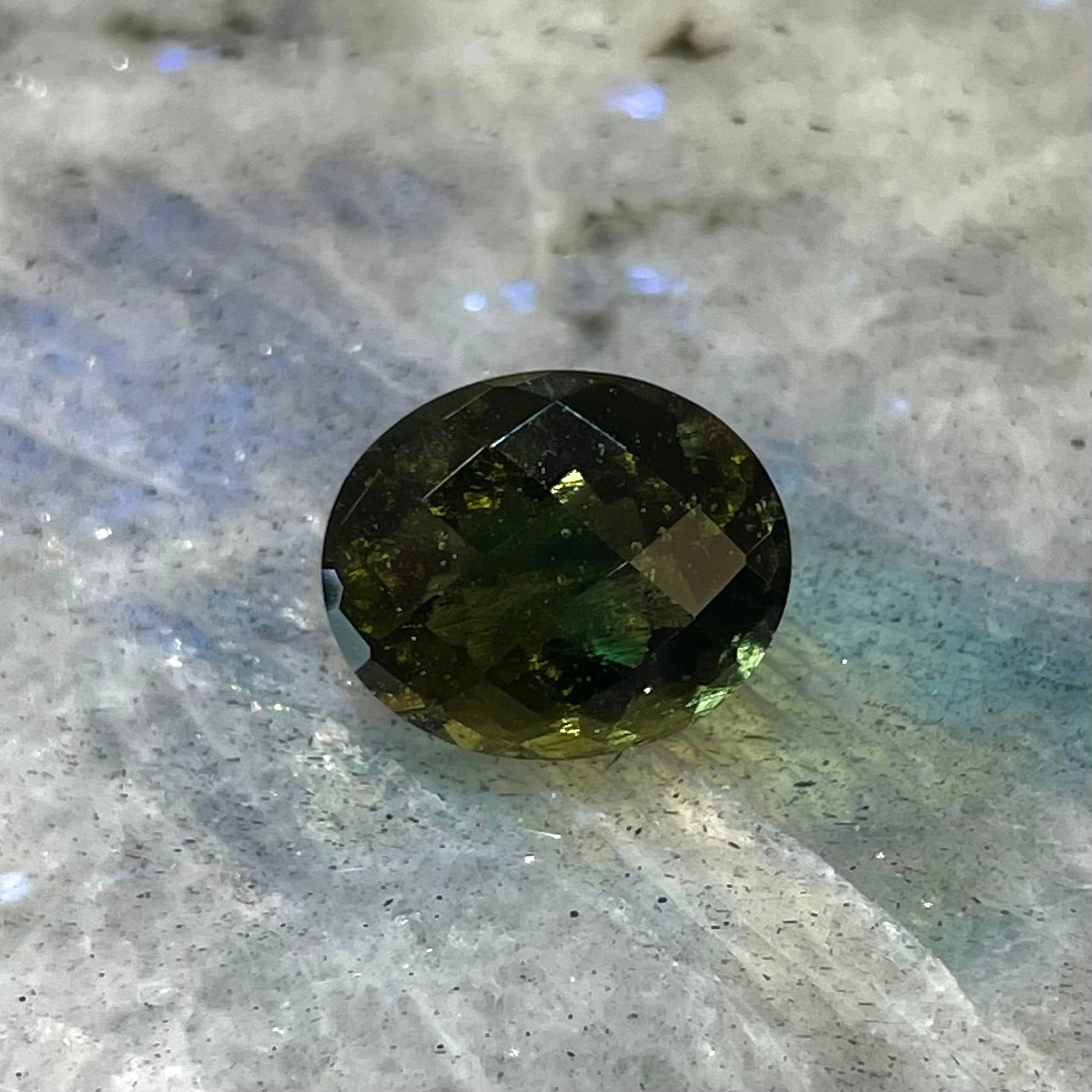 A faceted oval checkerboard cut moldavite gemstone that weighs 4.14 carats.