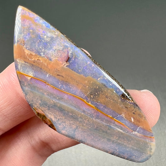 A polished boulder opal stone from Queensland, Australia.  There is an orange stripe of matrix running through the purple opal.