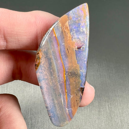 A polished boulder opal stone from Queensland, Australia.  There is an orange stripe of matrix running through the purple opal.