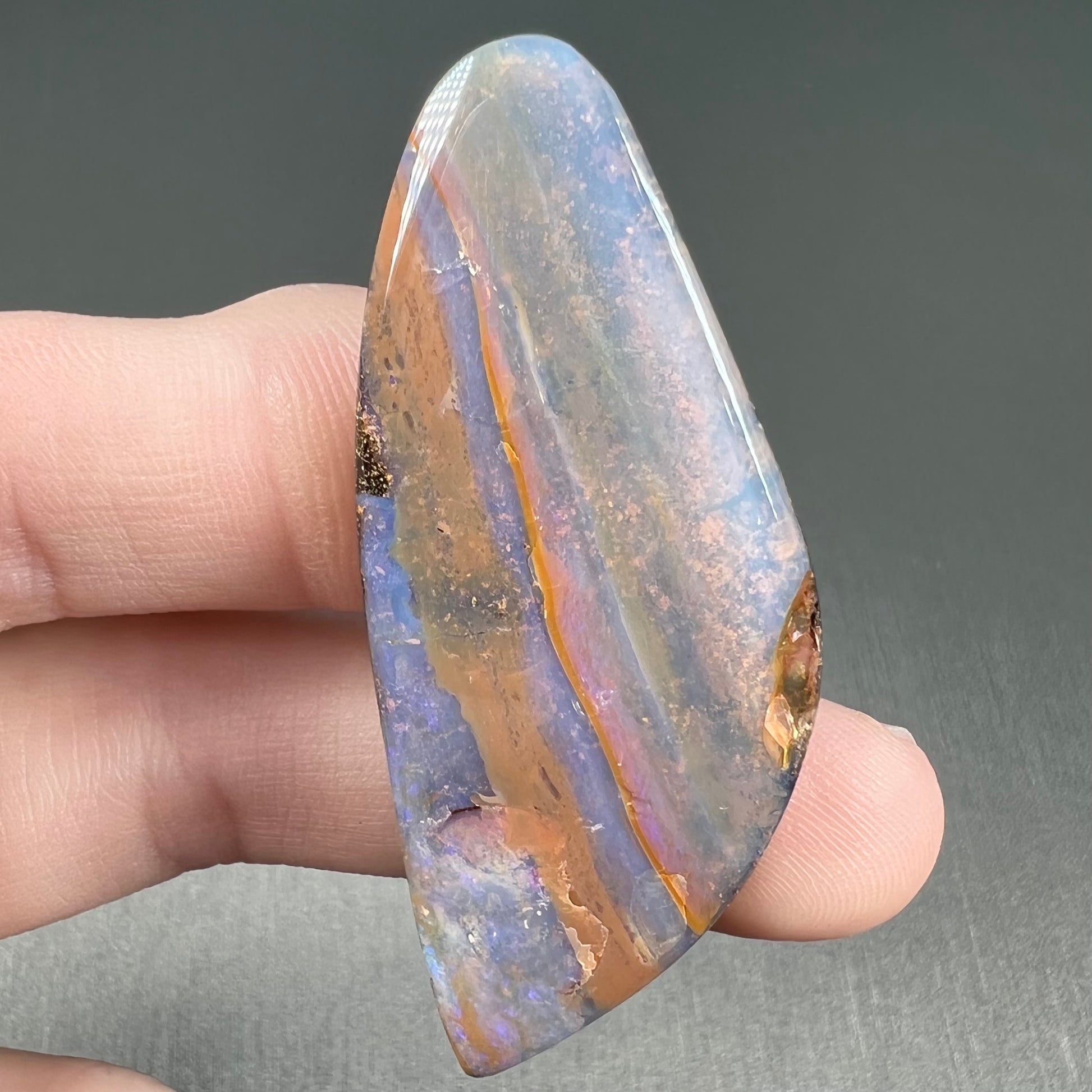 A polished boulder opal stone from Queensland, Australia.  There is an orange stripe of matrix running through the purple opal.