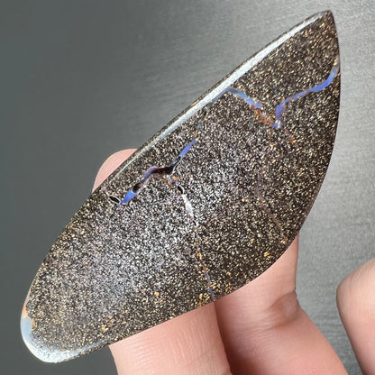 A polished boulder opal stone from Queensland, Australia.  There is an orange stripe of matrix running through the purple opal.