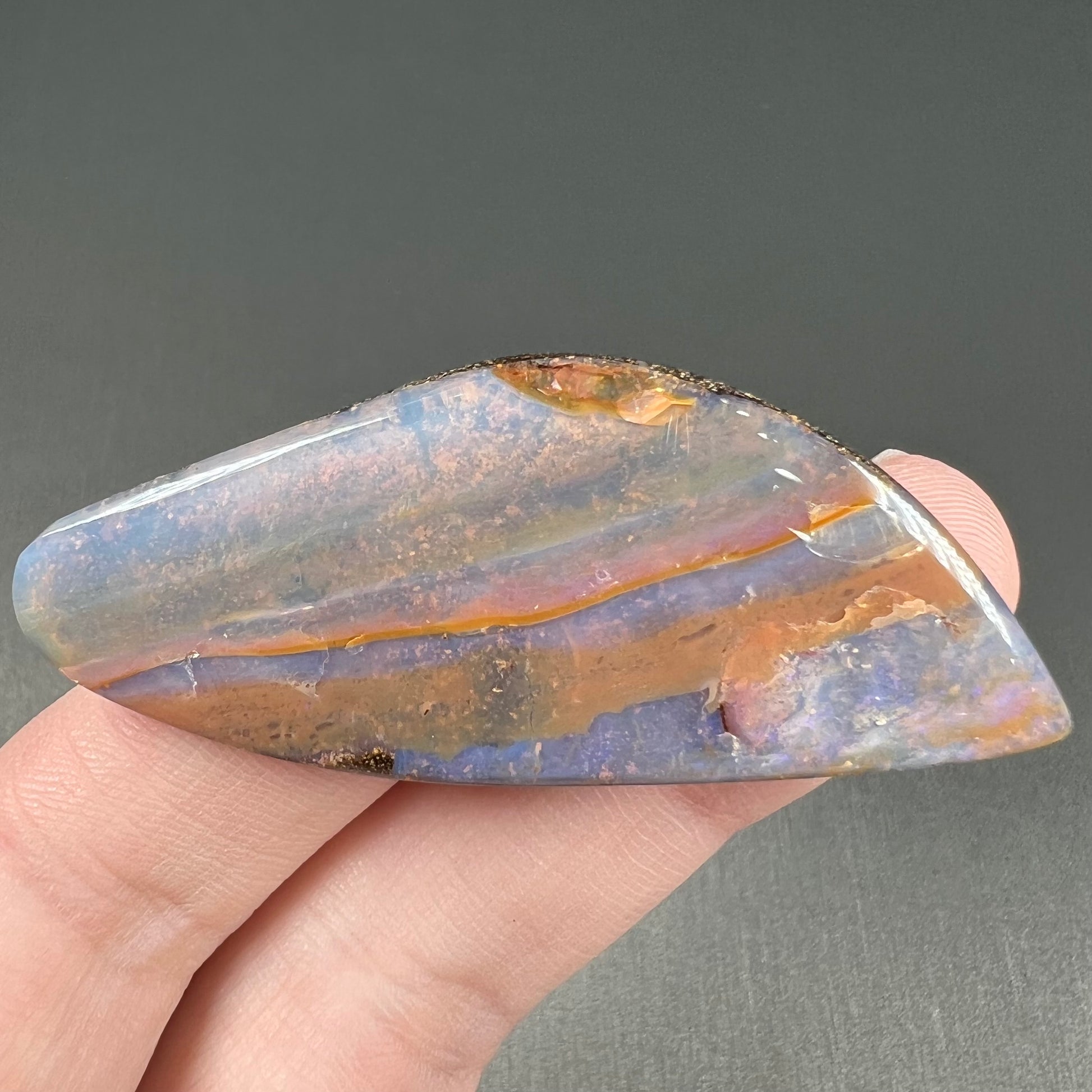 A polished boulder opal stone from Queensland, Australia.  There is an orange stripe of matrix running through the purple opal.
