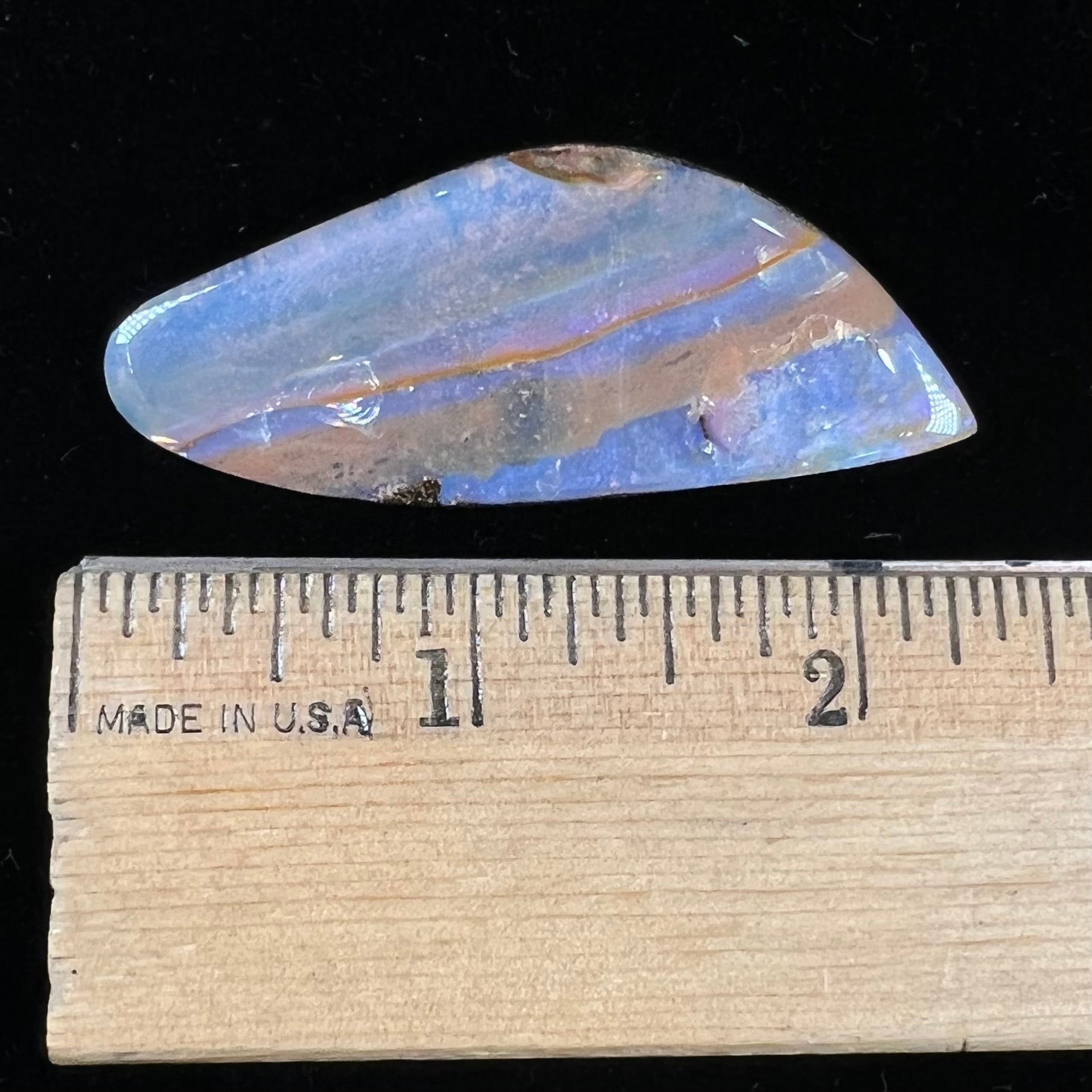 A polished boulder opal stone from Queensland, Australia.  There is an orange stripe of matrix running through the purple opal.