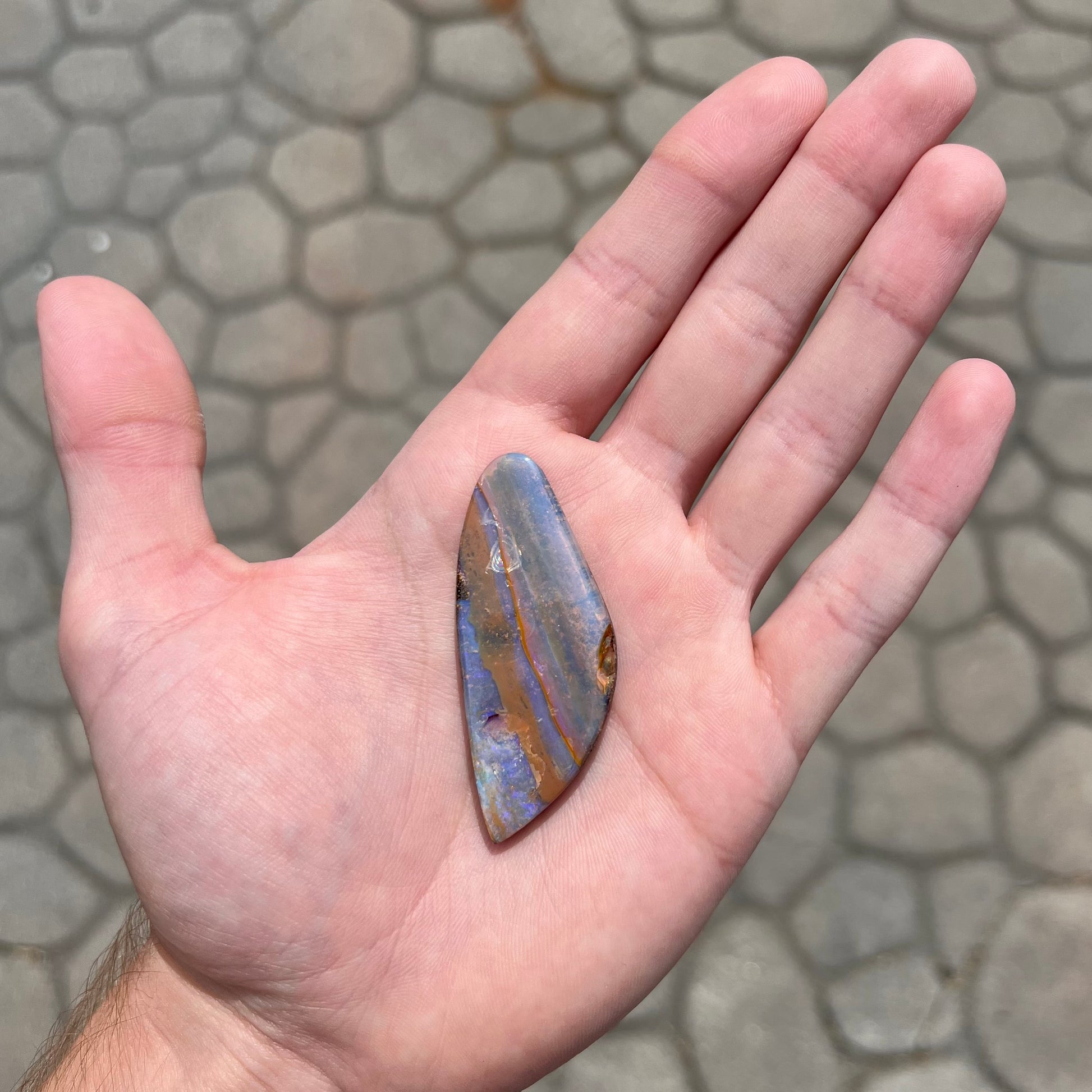A polished boulder opal stone from Queensland, Australia.  There is an orange stripe of matrix running through the purple opal.