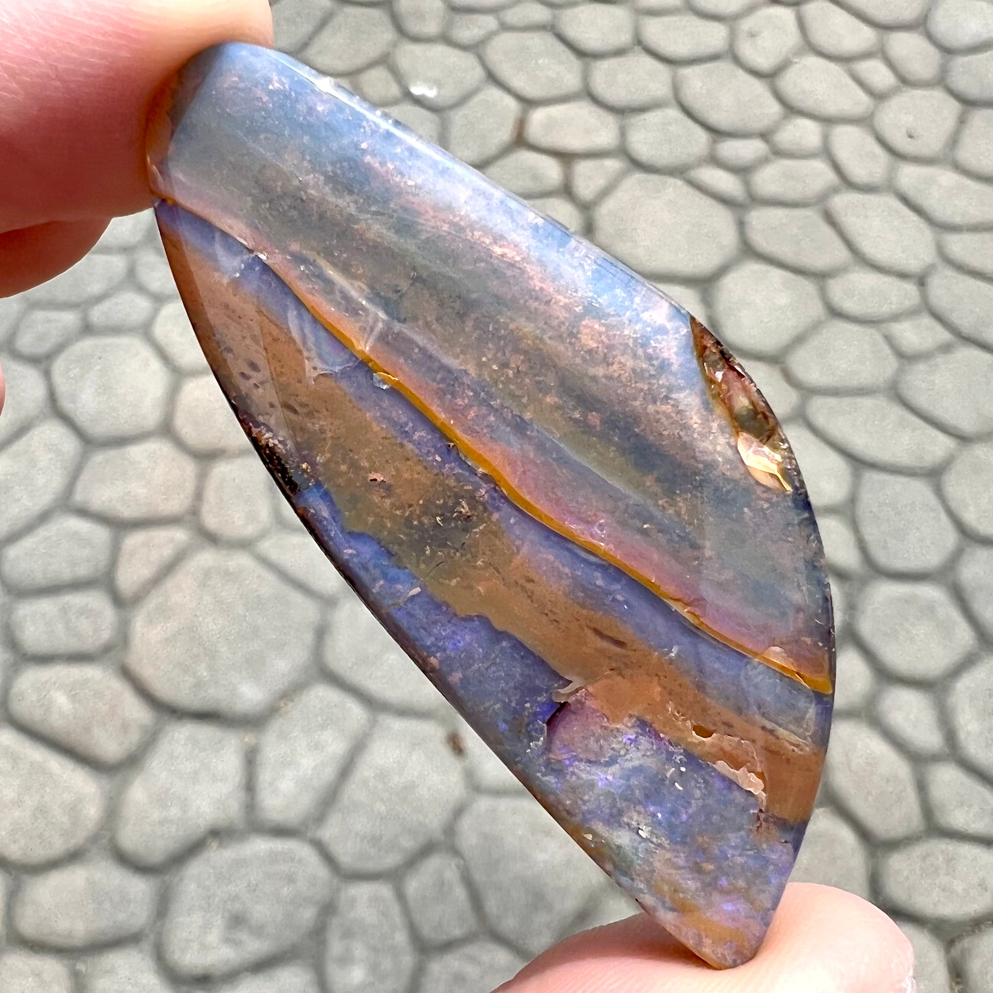 A polished boulder opal stone from Queensland, Australia.  There is an orange stripe of matrix running through the purple opal.