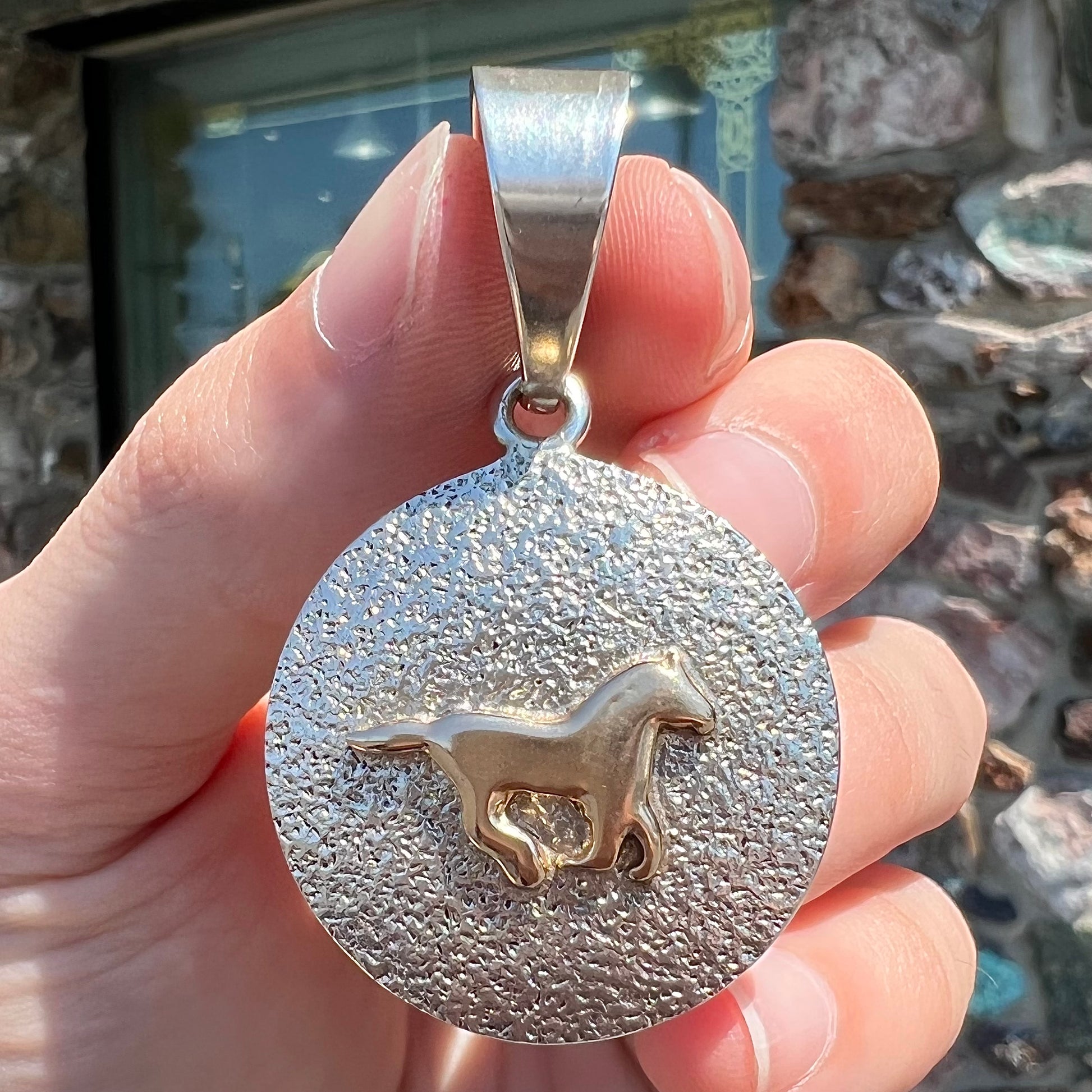 A Navajo-made sterling silver pendant depicting a yellow gold horse galloping.