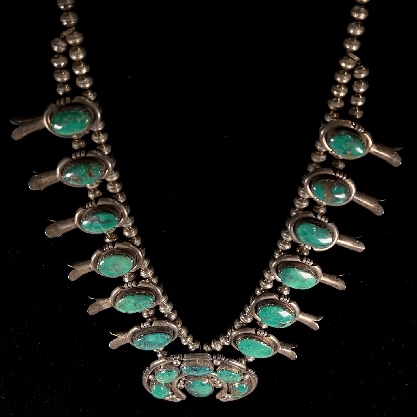A silver Kingman turquoise squash blossom necklace.  The necklace is made with handmade Navajo pearls.
