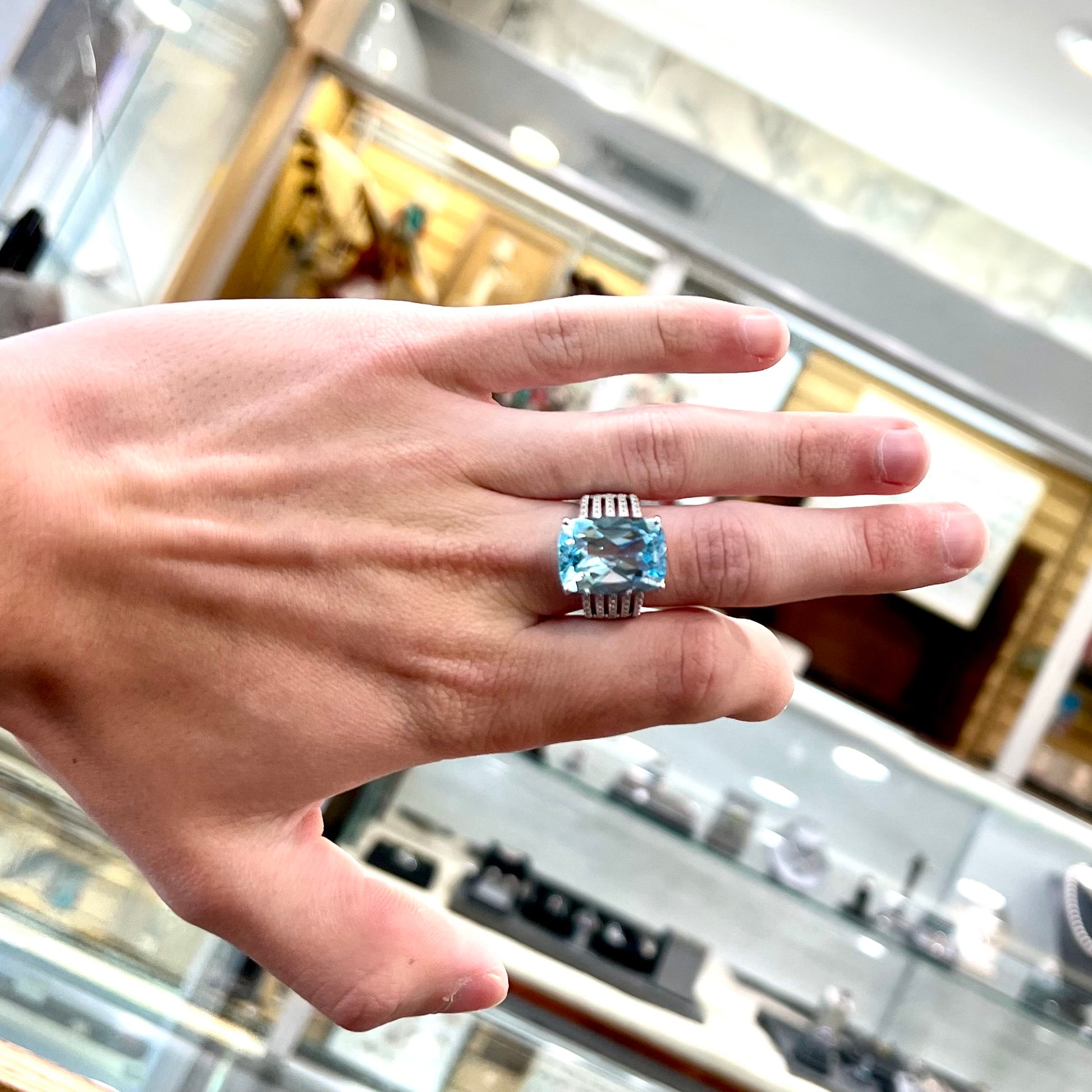 A sterling silver ring prong set with a large, cushion cut sky blue topaz stone.  The shank has been textured to mimic accent stones.