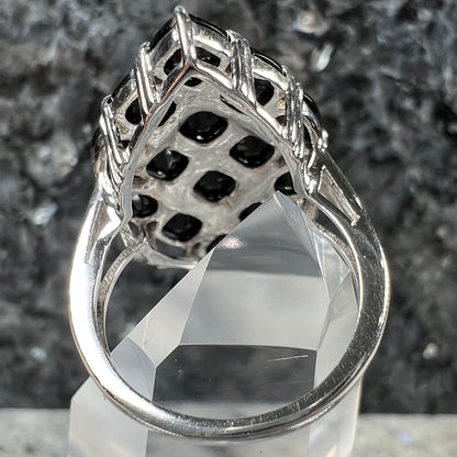 A sterling silver ring cluster set with faceted black spinel stones set to form a marquise shape.
