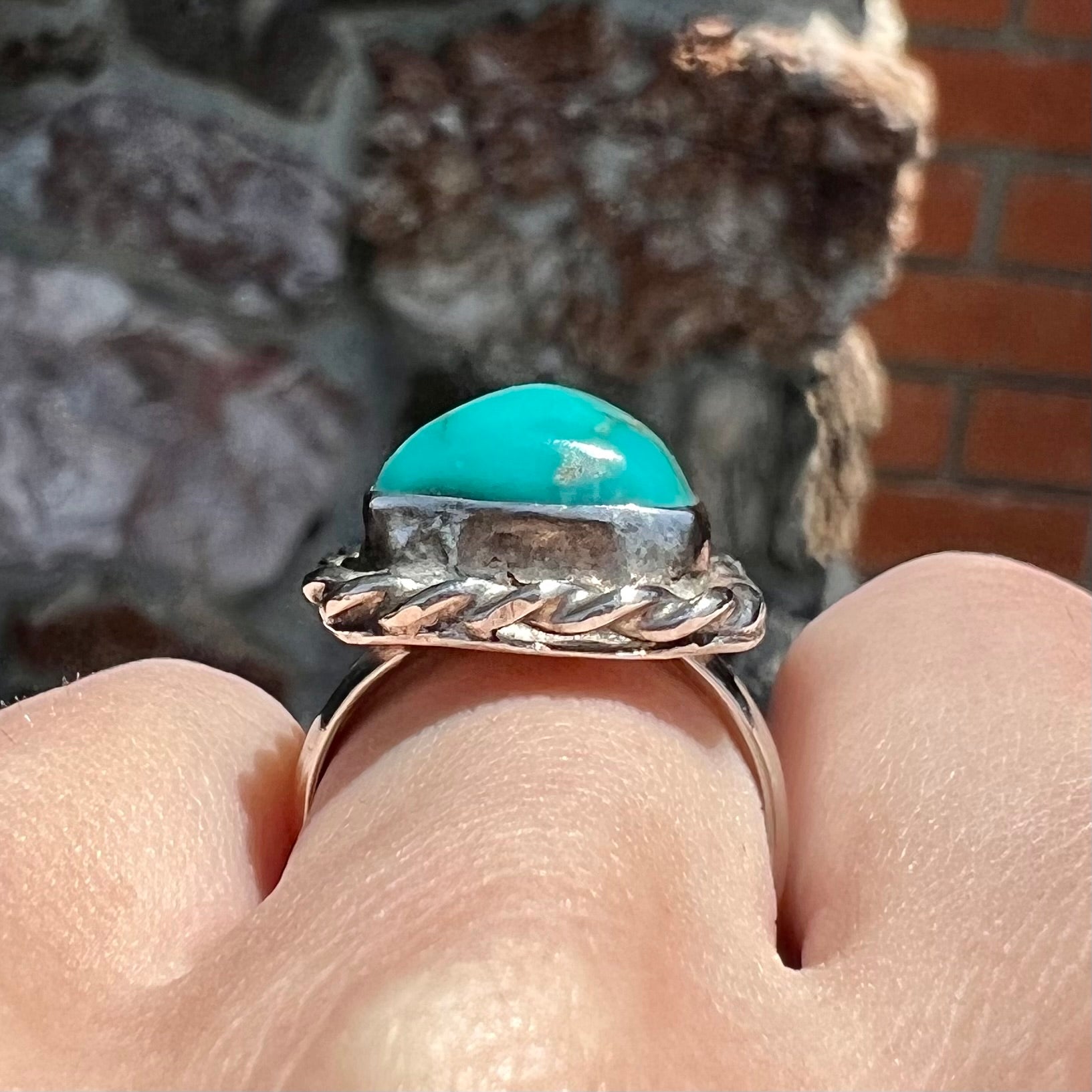 A sterling silver turquoise split shank ring.  There is a handmade silver rope around the turquoise.