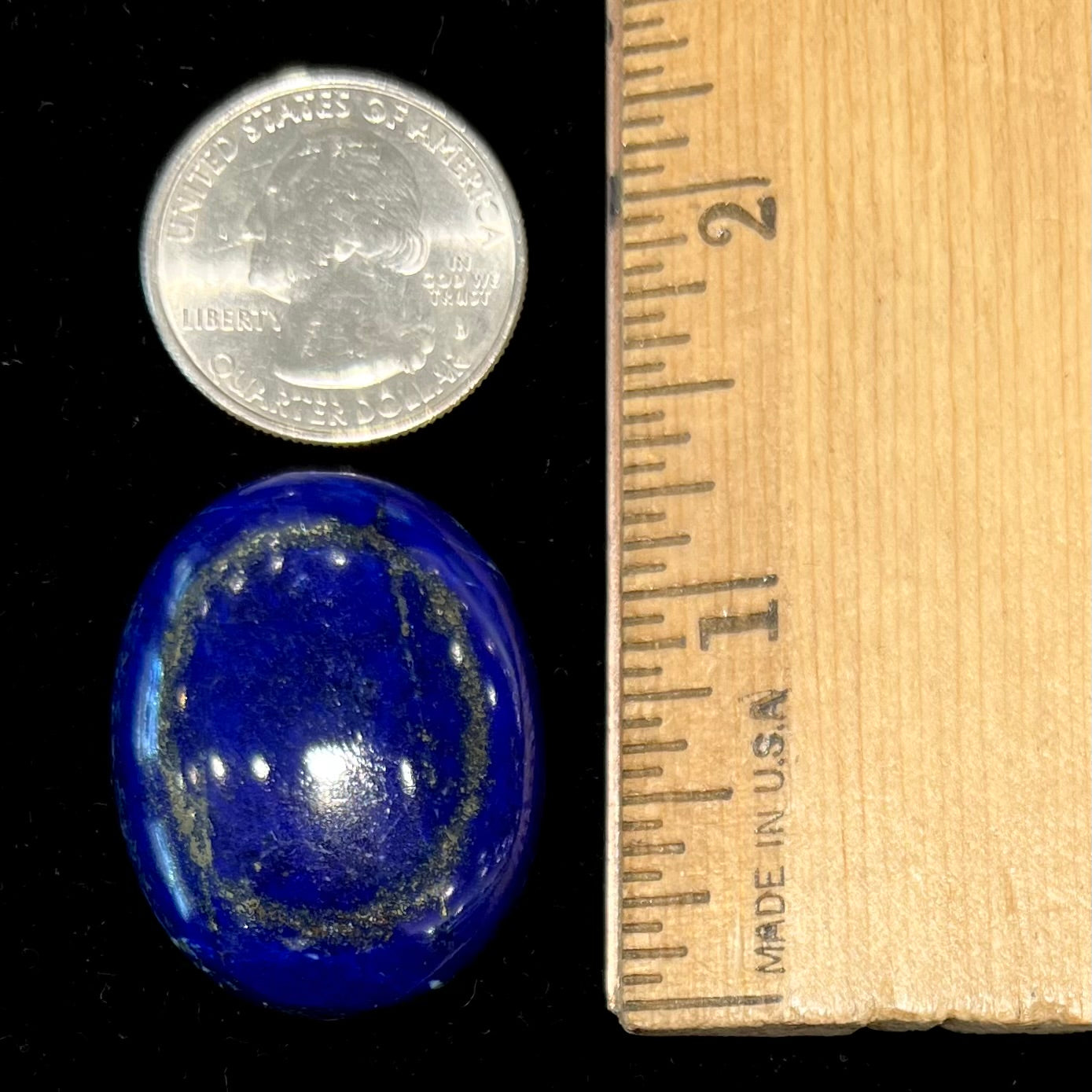 A loose, oval cabochon cut lapis lazuli stone.  A circle of pyrite inclusions is seen on the front.