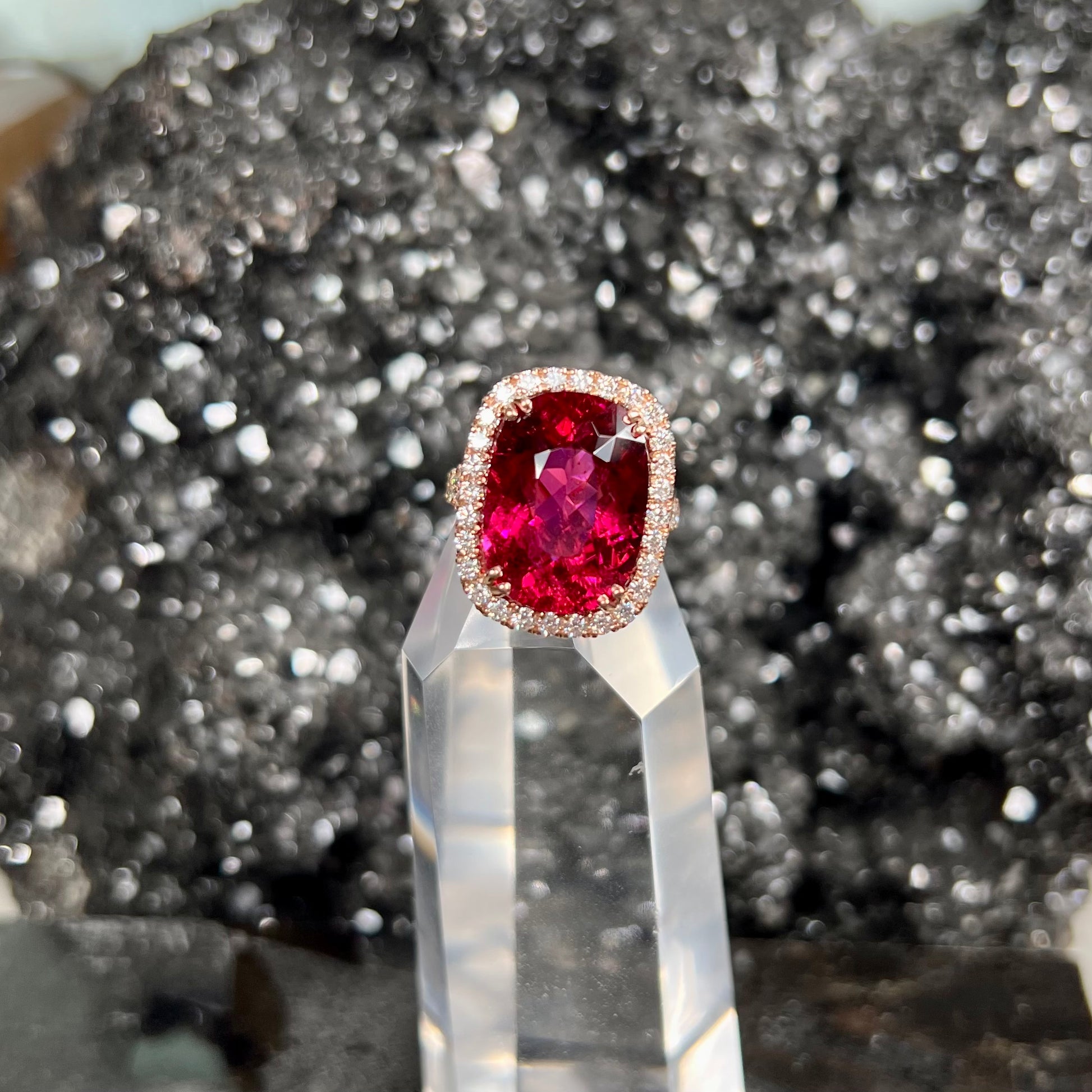 A rose gold, split shank engagement ring set with a cushion cut rubellite tourmaline in a diamond halo.