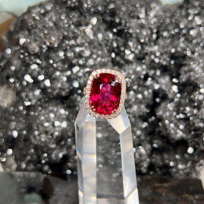 A rose gold, split shank engagement ring set with a cushion cut rubellite tourmaline in a diamond halo.