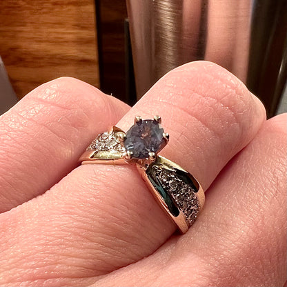 Natural alexandrite set in six prong yellow gold setting with pave diamonds.  The ring is under orange incandescent light.