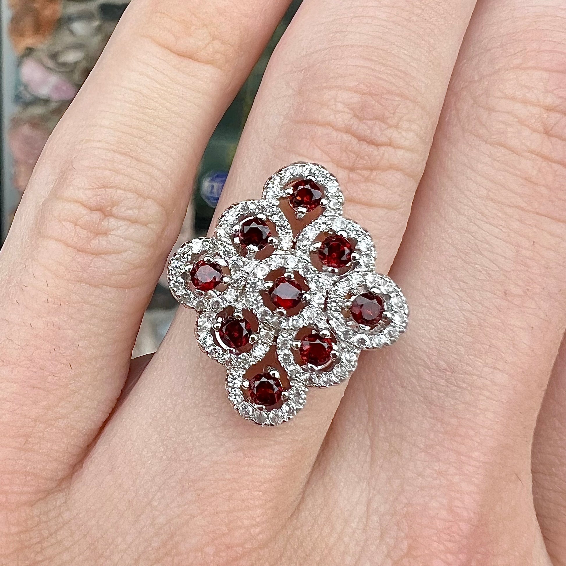 A sterling silver cluster ring set with round almandine garnet main stones and white zircon accents.