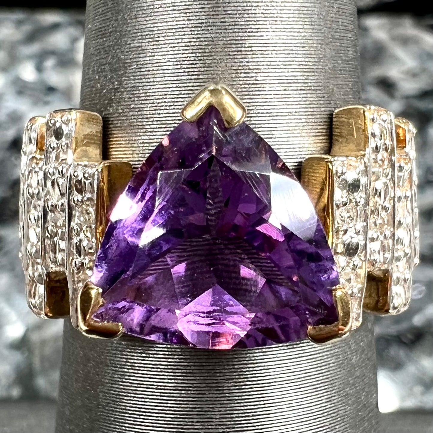 A yellow gold ring set with a trillion cut amethyst and round diamond accent stones.