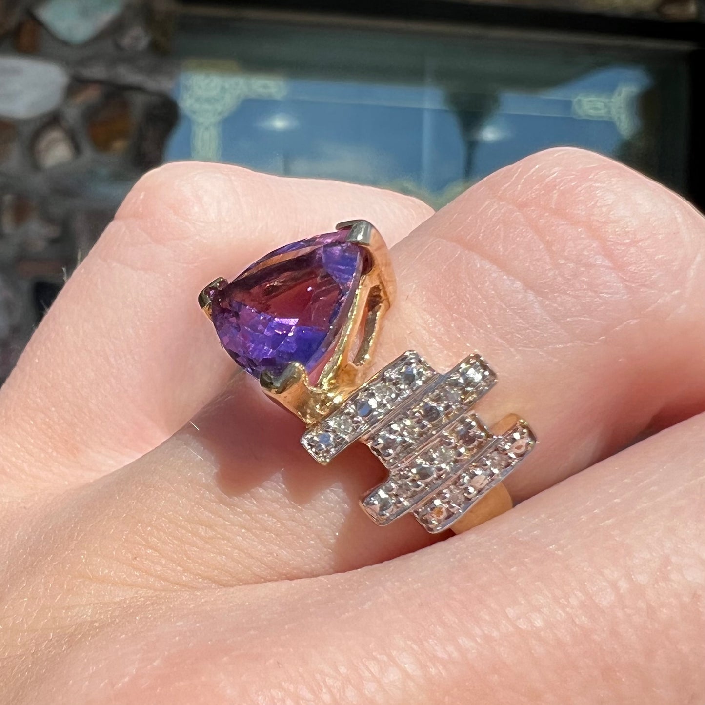 A yellow gold ring set with a trillion cut amethyst and round diamond accent stones.