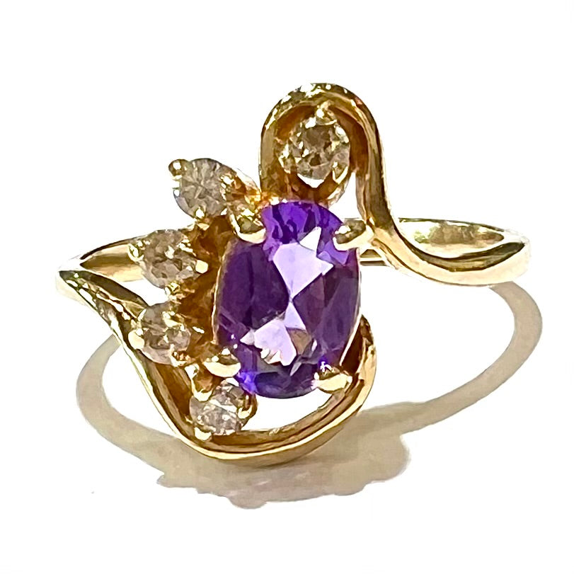 A ring made with 14 karat yellow gold, diamonds, and an amethyst.  The ring has a swoosh style.