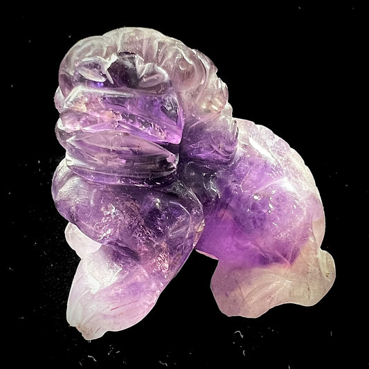 A stone foo dog carving carved from a purple Brazilian amethyst crystal.