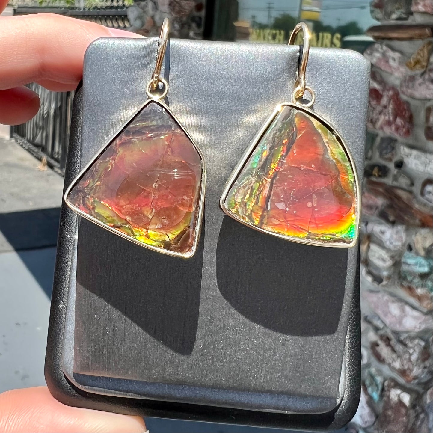 Yellow gold French wire dangle earrings bezel set with two polished freeform cut red ammolite fossils.