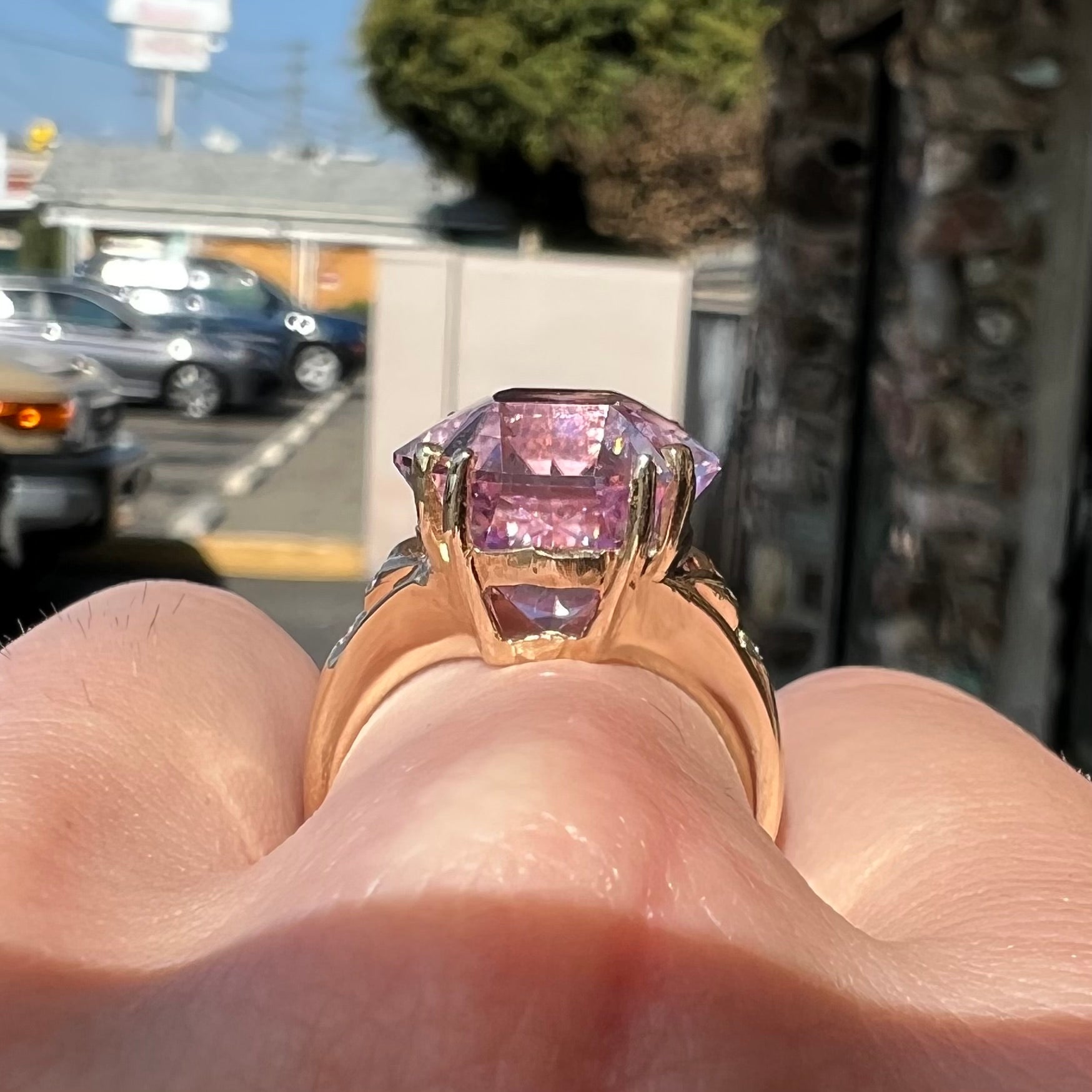 A large, pink kunzite is prong set into a 14kt yellow gold basket-style ring mounting with three diamonds flush set into the design on each side.