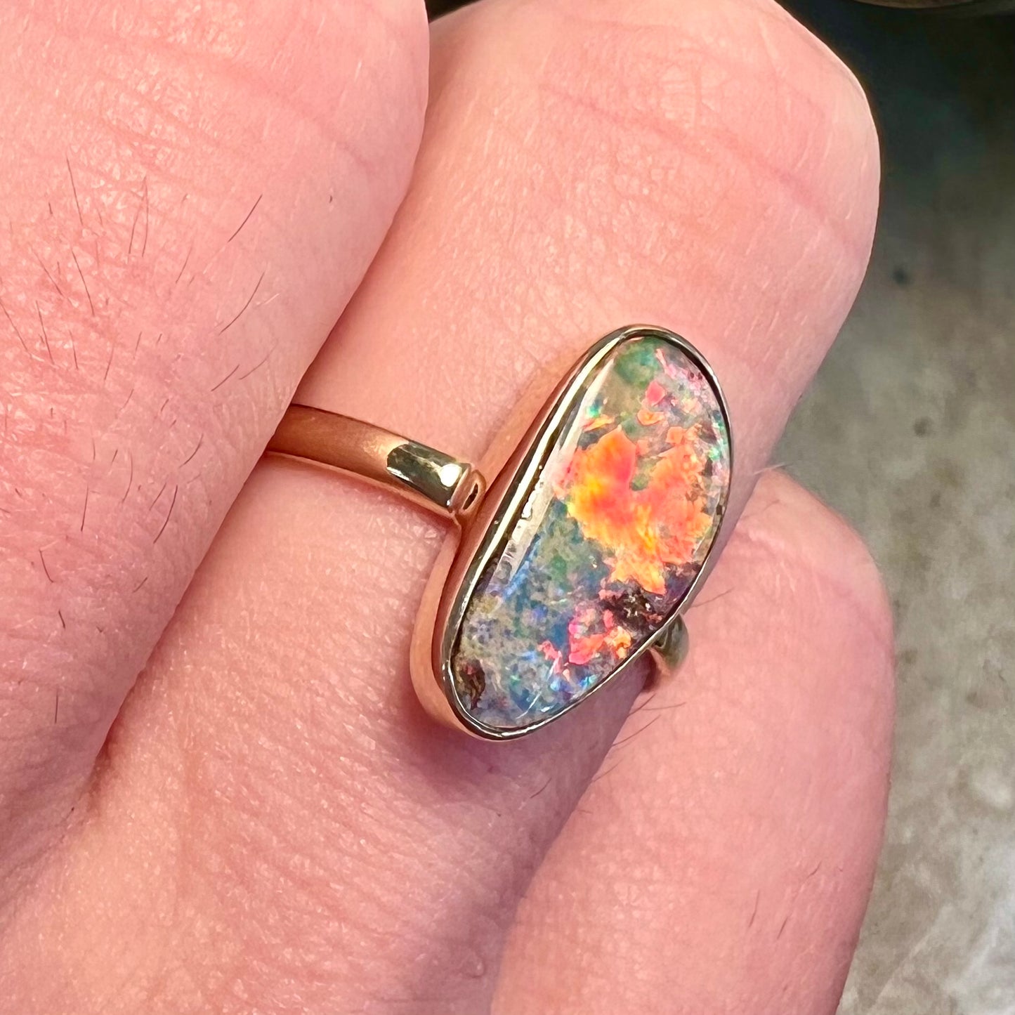A bright, freeform cabochon cut rainbow boulder opal set in a yellow gold solitaire ring.