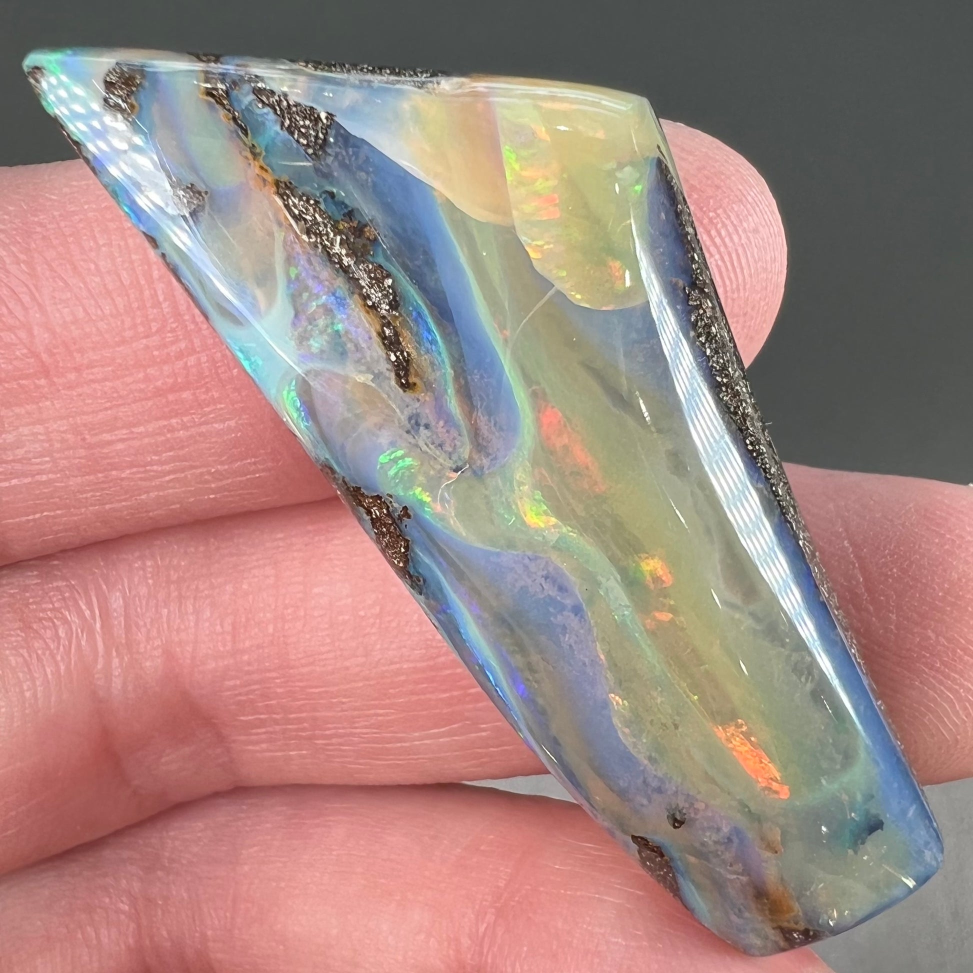 A freeform shaped, polished boulder opal stone from Queensland, Australia.  The stone has red, orange, green, and blue fire.