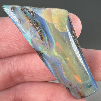 A freeform shaped, polished boulder opal stone from Queensland, Australia.  The stone has red, orange, green, and blue fire.