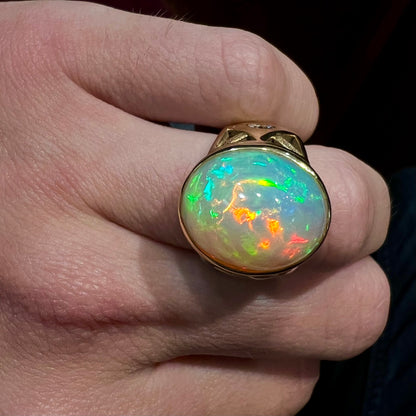 A custom yellow gold men's ring set with two diamonds and a large oval cabochon cut opal from Ethiopia, Africa.