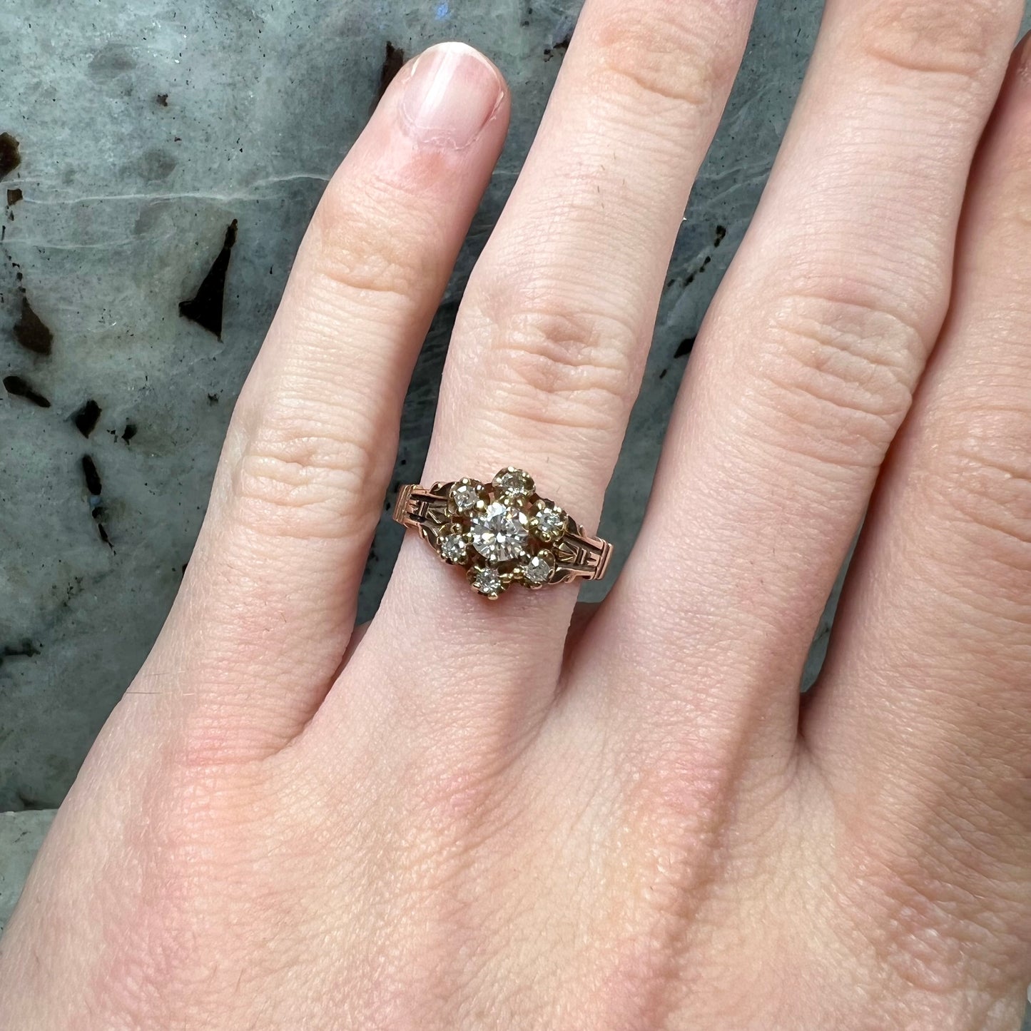A modern Standard Round Brilliant Cut diamond set between six smaller round diamonds in an antique rose gold engagement ring setting.
