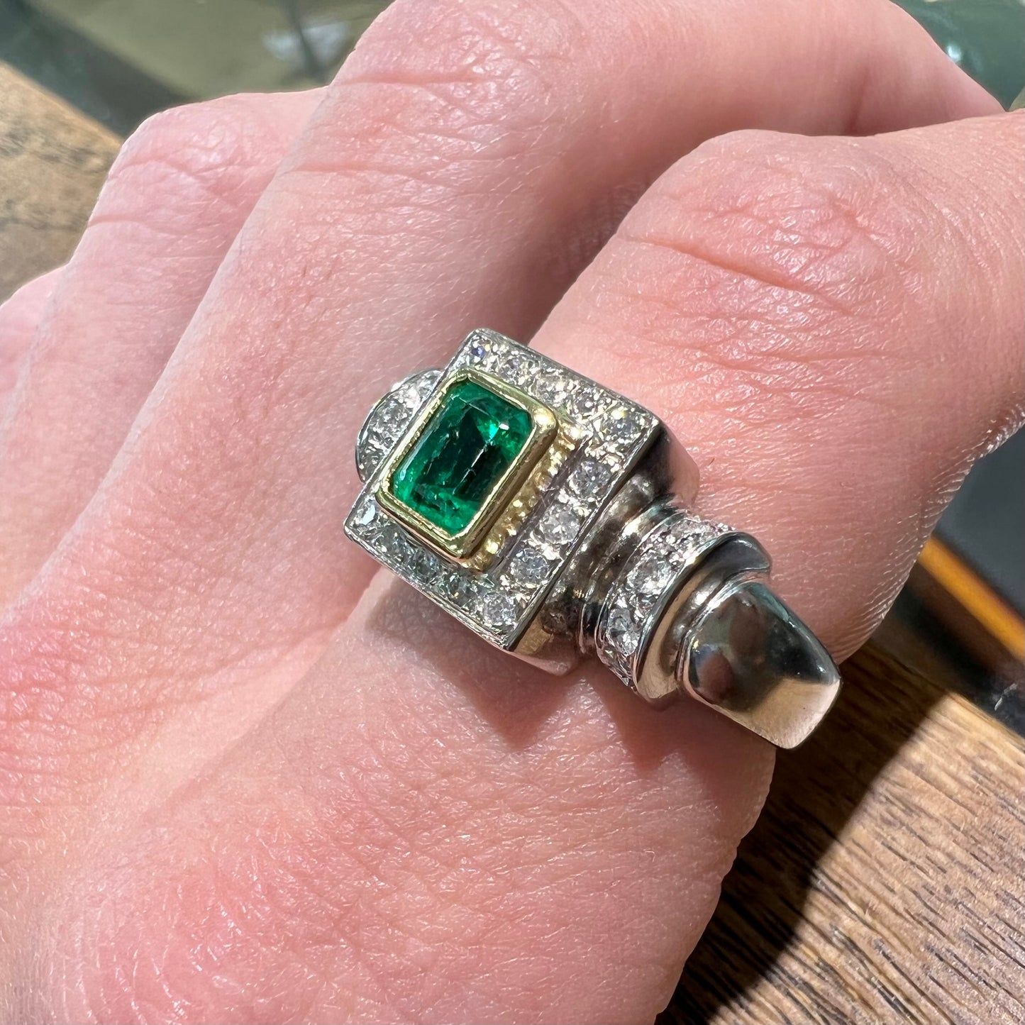 A two tone gold emerald and diamond halo ring.