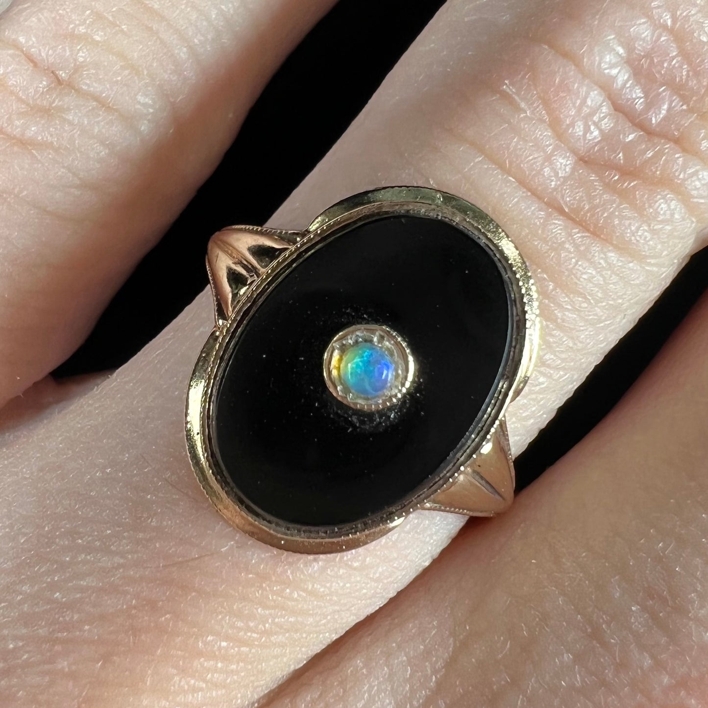 A yellow gold onyx ring set with a round cabochon cut opal bezel set into the onyx.