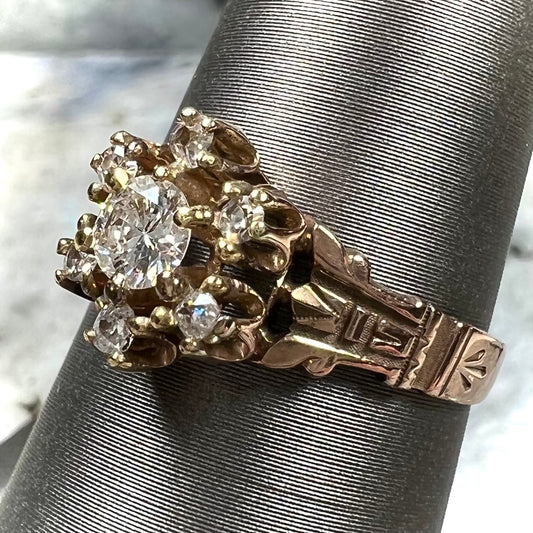 A modern Standard Round Brilliant Cut diamond set between six smaller round diamonds in an antique rose gold engagement ring setting.