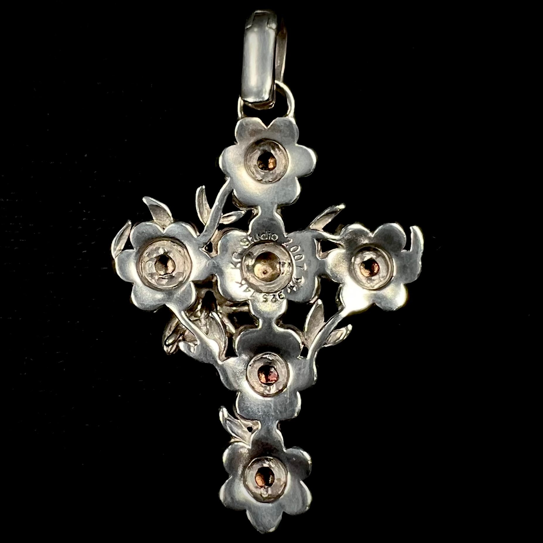 A cross pendant with floral decoration.  The cross is made of six  flowers with sterling silver petals and yellow gold nectar.  A silver bee is on one of the pendants.  The bail opens and closes.