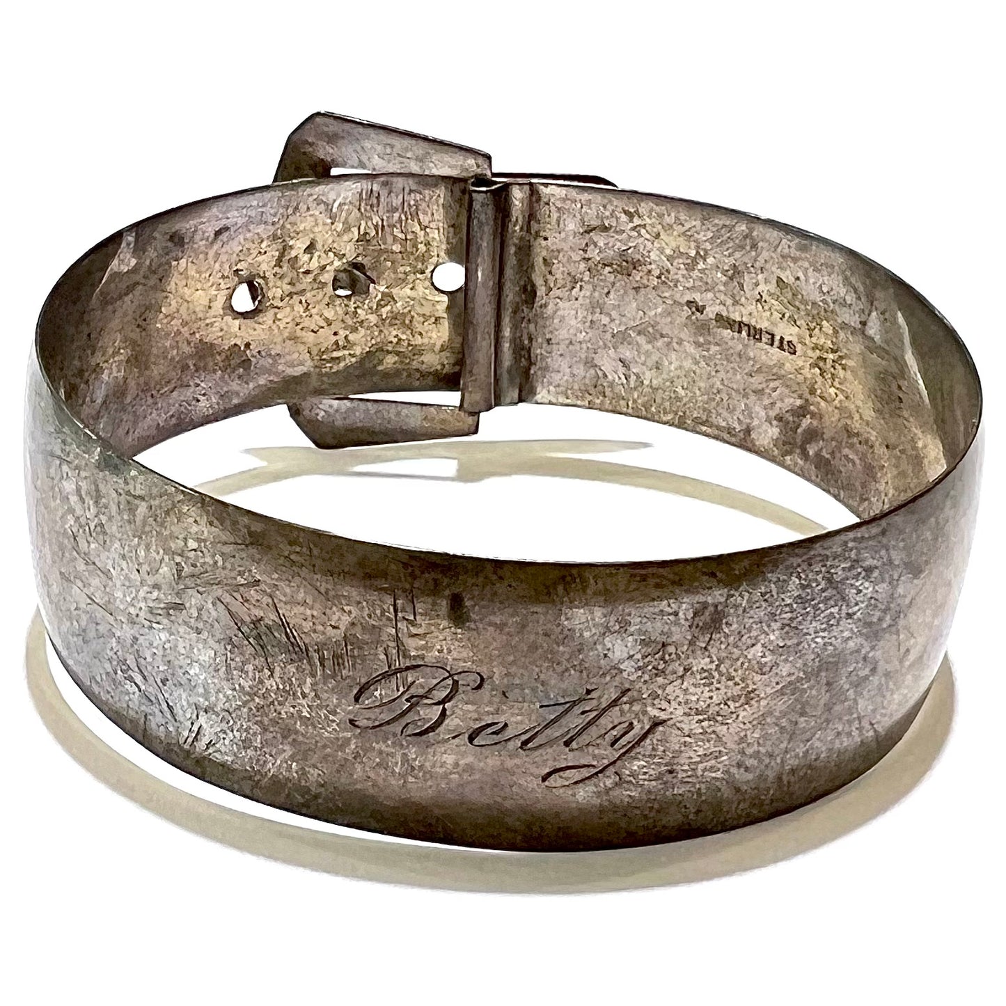 The underside of a worn buckle-motif style metal bracelet.  The word "STERLING" is stamped inside of the piece, and the name "Betty" is engraved in script letters on the bottom outside of the bracelet.
