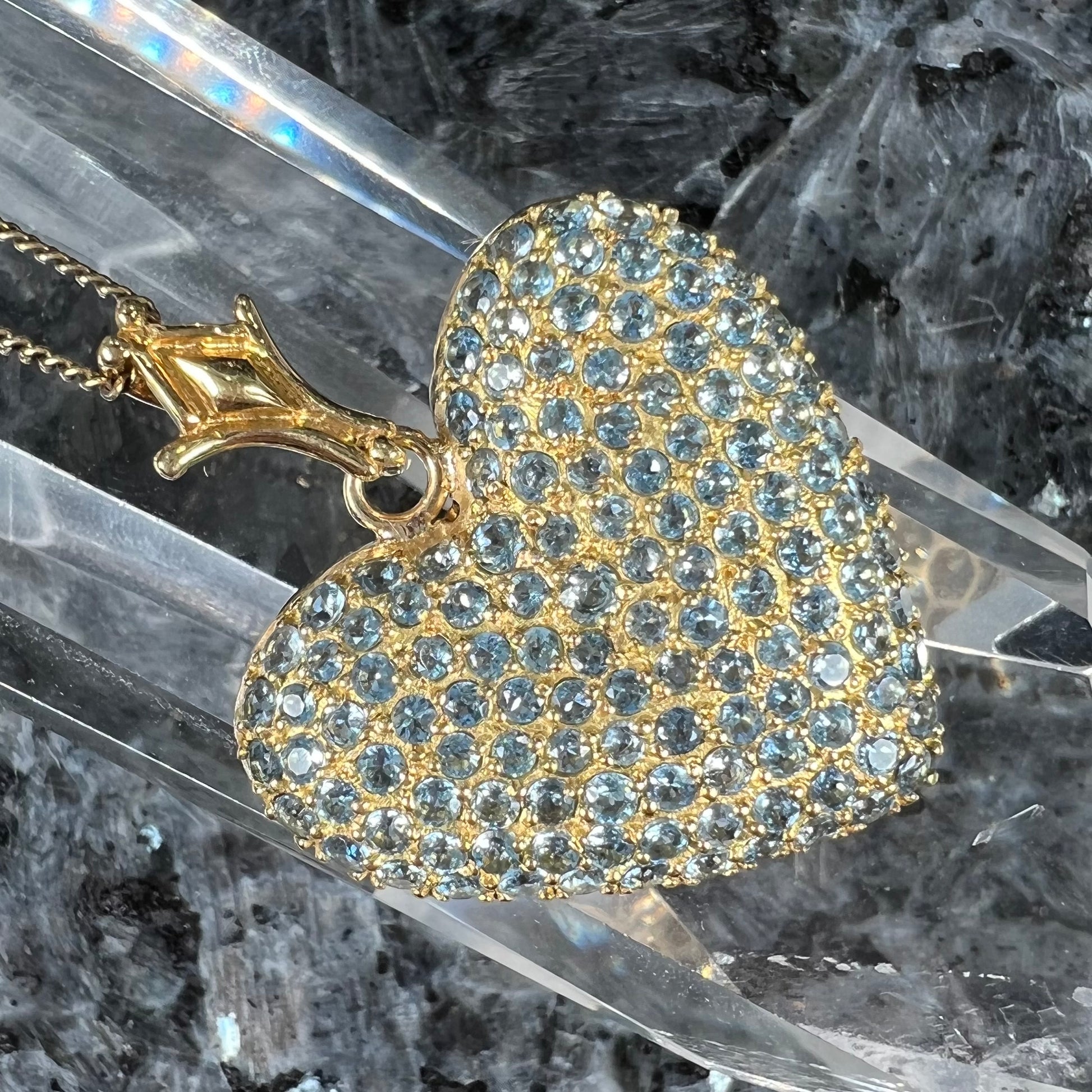 A gold heart pendant pave set with round aquamarine stones.