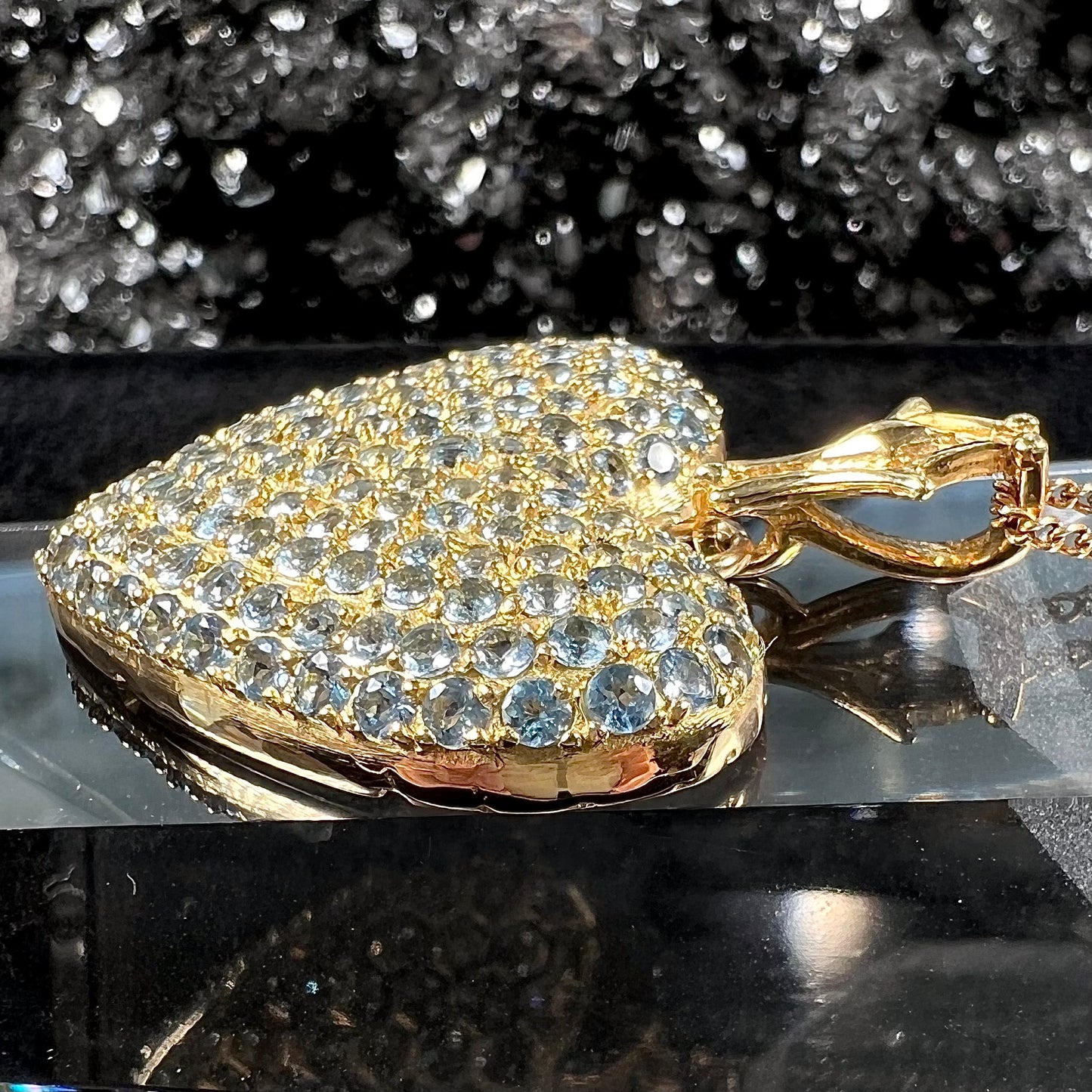 A gold heart pendant pave set with round aquamarine stones.