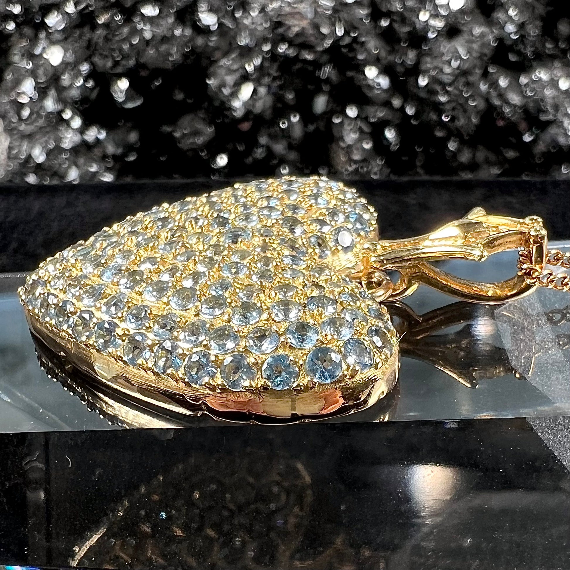 A gold heart pendant pave set with round aquamarine stones.