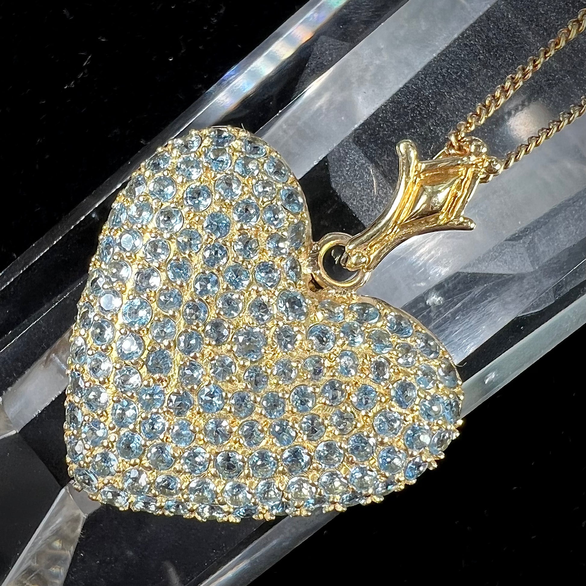 A gold heart pendant pave set with round aquamarine stones.