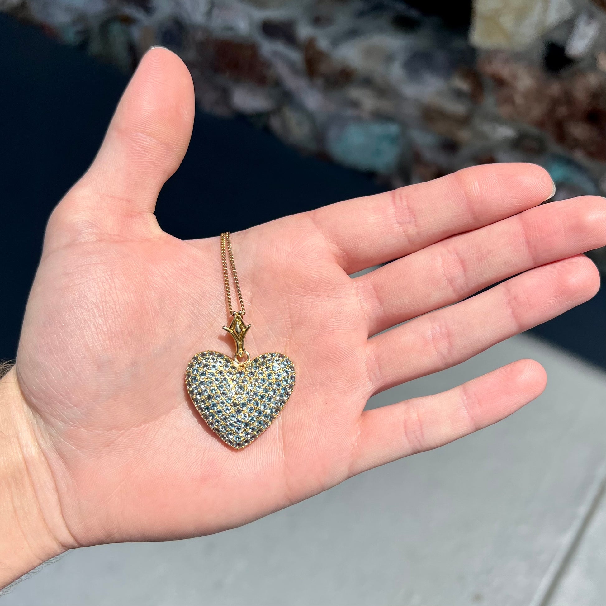 A gold heart pendant pave set with round aquamarine stones.