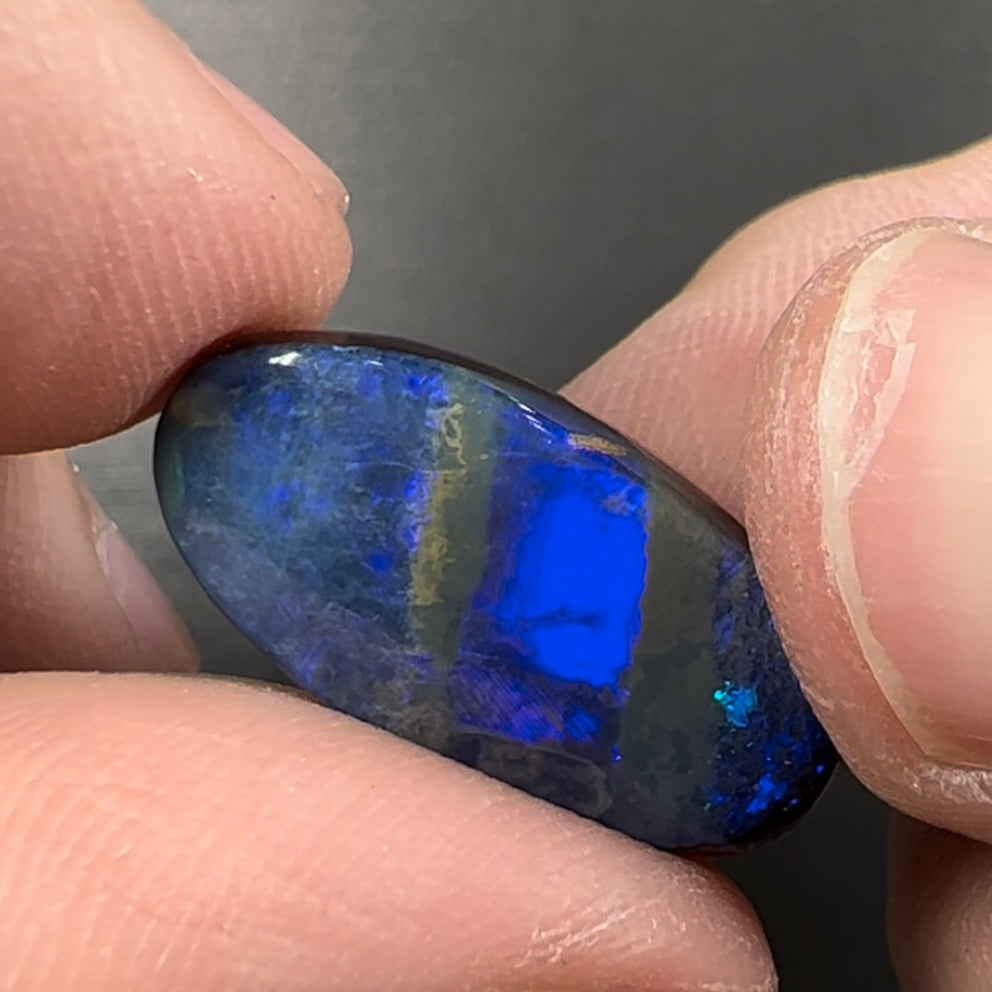 A loose, oval cabochon cut black boulder opal stone from Quilpie, Australia.