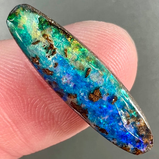 A loose, oval cabochon cut Australian boulder opal from Quilpie, Australia.  Predominant colors are blue and green.