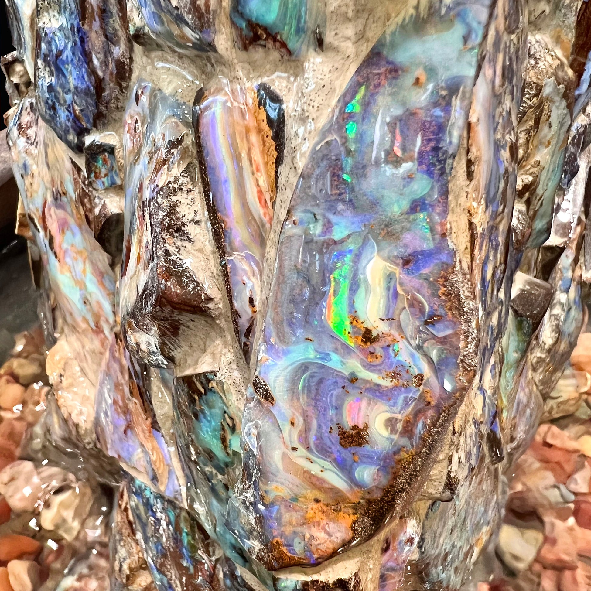 An indoor/outdoor three sided pyramid fountain made from Australian boulder opal, sitting in a bowl of Mexican fire opal.